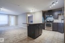 Open-concept kitchen featuring dark cabinetry, stainless steel appliances, and a central island with countertop seating - 201 1520 Hammond Gate Gate, Edmonton, AB  - Indoor Photo Showing Kitchen With Stainless Steel Kitchen 