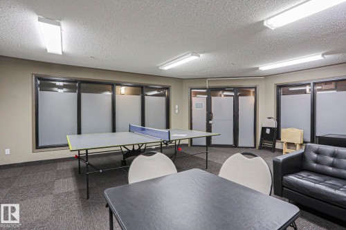 Recreation room featuring textured carpet flooring, multiple frosted window panels, and recessed fluorescent lighting - 201 1520 Hammond Gate Gate, Edmonton, AB - Indoor Photo Showing Other Room
