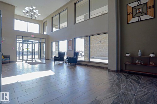 Spacious lobby featuring high ceilings, extensive window lighting, and a multi-tiered chandelier - 201 1520 Hammond Gate Gate, Edmonton, AB - Indoor Photo Showing Other Room