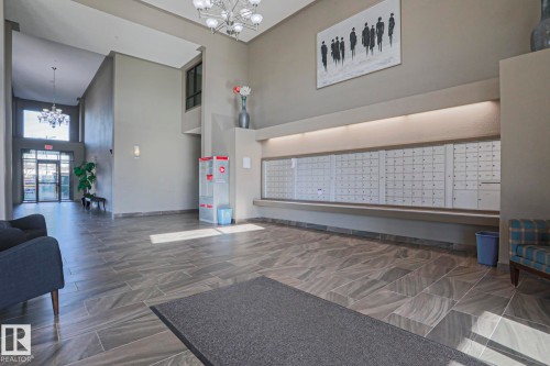 Spacious main lobby featuring large format tile flooring, a comprehensive wall-mounted mailbox system, and a double-height ceiling in the entry vestibule - 201 1520 Hammond Gate Gate, Edmonton, AB - Indoor Photo Showing Other Room