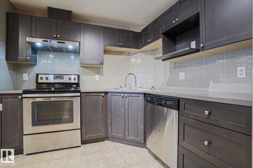 Kitchen featuring dark wood-finish cabinetry, stainless steel appliances, light-toned countertops, and a subway tile backsplash - 201 1520 Hammond Gate Gate, Edmonton, AB - Indoor Photo Showing Kitchen With Stainless Steel Kitchen