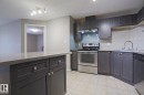 Contemporary kitchen featuring dark cabinetry, stainless steel appliances, a light-colored tile backsplash, and a breakfast bar with a solid surface countertop - 201 1520 Hammond Gate Gate, Edmonton, AB  - Indoor Photo Showing Kitchen With Stainless Steel Kitchen 