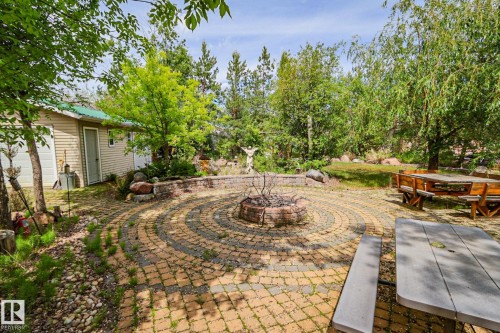 Expansive outdoor patio featuring a circular paver design, a central fire pit, and a stone retaining wall - 400 60501 Range Road 120, Rural St. Paul County, AB - Outdoor