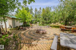 Expansive outdoor patio featuring a circular paver design, a central fire pit, and a stone retaining wall - 