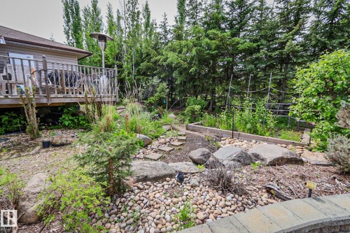 Expansive outdoor space featuring a raised garden bed, natural rock landscaping, pebble pathways, mature evergreen trees, and a wooden deck - 400 60501 Range Road 120, Rural St. Paul County, AB - Outdoor