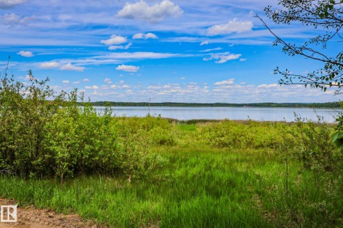 Expansive natural waterfront setting featuring abundant green foliage, a tranquil body of water, and a clear blue sky with scattered clouds - 400 60501 Range Road 120, Rural St. Paul County, AB - Outdoor With Body Of Water With View