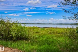 Expansive natural waterfront setting featuring abundant green foliage, a tranquil body of water, and a clear blue sky with scattered clouds - 