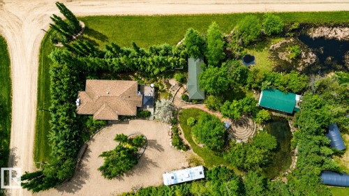 Expansive property featuring a main residence with a brown shingle roof, multiple outbuildings with green roofs, a natural pond, and mature landscaping - 400 60501 Range Road 120, Rural St. Paul County, AB - Outdoor With View