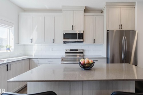 Contemporary kitchen featuring a large central island with a solid surface countertop, white shaker-style cabinetry, stainless steel appliances, white subway tile backsplash, and a window above the sink - 5237 Edgemont Boulevard, Edmonton, AB - Indoor Photo Showing Kitchen With Stainless Steel Kitchen With Double Sink With Upgraded Kitchen