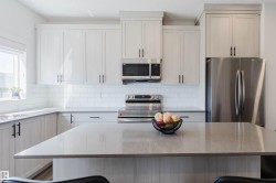 Contemporary kitchen featuring a large central island with a solid surface countertop, white shaker-style cabinetry, stainless steel appliances, white subway tile backsplash, and a window above the sink - 