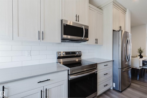 Kitchen featuring light-toned cabinetry with black hardware, subway tile backsplash, stainless steel appliances, and a light-colored countertop - 5237 Edgemont Boulevard, Edmonton, AB - Indoor Photo Showing Kitchen With Stainless Steel Kitchen With Upgraded Kitchen