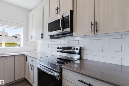 Modern kitchen featuring light wood-finish cabinetry with black hardware, stainless steel appliances, a white subway tile backsplash, and light-toned countertops - 5237 Edgemont Boulevard, Edmonton, AB - Indoor Photo Showing Kitchen With Upgraded Kitchen