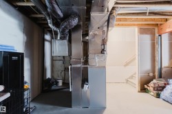 Unfinished basement space featuring exposed joists and framing, with visible HVAC ductwork and utility lines - 