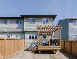 Rear exterior featuring a wood deck with pergola, black metal railings, and a privacy fence - 