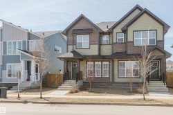 Duplex exterior featuring light green siding, dark brown shake siding accents, multiple white-framed windows, and a covered entry with a dark green door - 