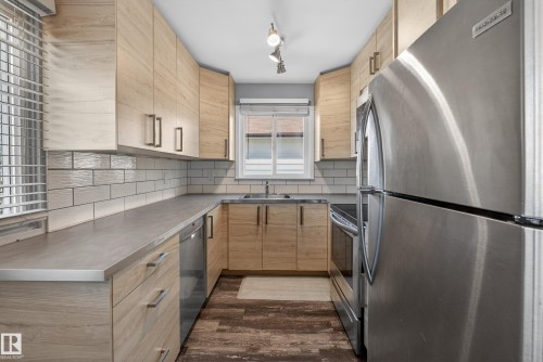 U-shaped kitchen featuring light wood-finish cabinetry with contemporary hardware, stainless steel appliances, a subway tile backsplash, and wood-finish flooring - 5 Linden St, Spruce Grove, AB - Indoor Photo Showing Kitchen With Double Sink