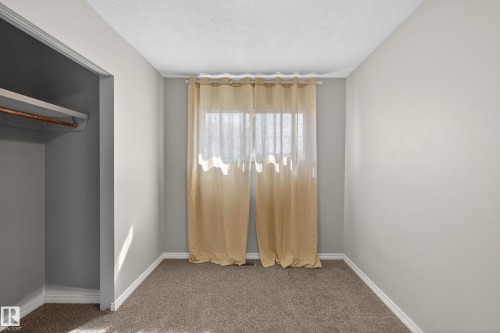 Carpeted room featuring a window with sheer curtains, a built-in closet with a hanging rod and shelf, light gray painted walls, and white baseboards - 5 Linden St, Spruce Grove, AB - Indoor