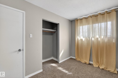 Carpeted room with neutral gray walls, a built-in closet with shelving and hanging rod, a white interior door, and a window with sheer curtains - 5 Linden St, Spruce Grove, AB - Indoor