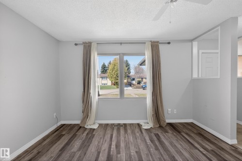 Spacious room featuring wood-finish flooring, a large window, light gray wall paint, and white trim - 5 Linden St, Spruce Grove, AB - Indoor Photo Showing Other Room