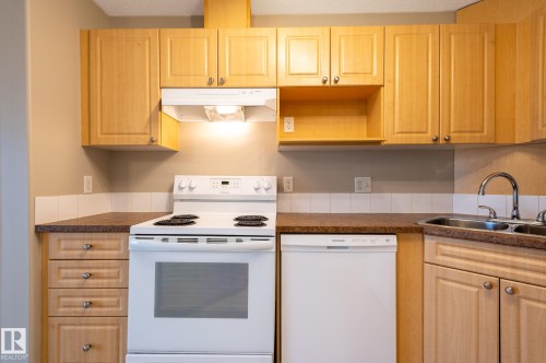 Kitchen featuring light wood-finish cabinetry, a white electric range with overhead exhaust fan, a white dishwasher, a dual basin stainless steel sink with gooseneck faucet, and laminate countertops - #314 240 Spruce Ridge Rd, Spruce Grove, AB - Indoor Photo Showing Kitchen With Double Sink
