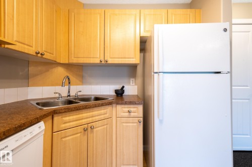 Kitchen featuring light wood-finish cabinetry, a double basin stainless steel sink with a high-arc faucet, and a white tile backsplash - #314 240 Spruce Ridge Rd, Spruce Grove, AB - Indoor Photo Showing Kitchen With Double Sink