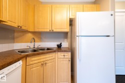 Kitchen featuring light wood-finish cabinetry, a double basin stainless steel sink with a high-arc faucet, and a white tile backsplash - 
