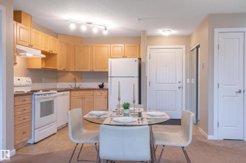 Open-concept living space with a U-shaped kitchen featuring wood cabinetry and white appliances - #314 240 Spruce Ridge Rd, Spruce Grove, AB - Indoor Photo Showing Kitchen