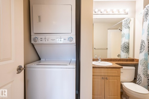 In-unit stacked laundry appliances and a full bathroom featuring a vanity with an integrated sink, stone-look countertop, and flush-mount lighting - #314 240 Spruce Ridge Rd, Spruce Grove, AB - Indoor Photo Showing Laundry Room