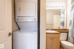 In-unit stacked laundry appliances and a full bathroom featuring a vanity with an integrated sink, stone-look countertop, and flush-mount lighting - 