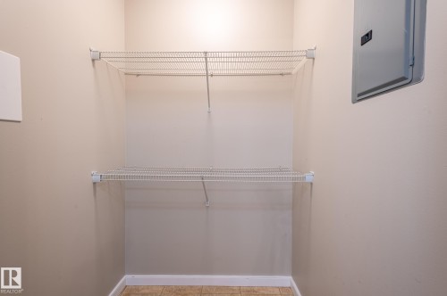 Compact utility space featuring neutral wall paint, two white wire shelving units, a gray electrical panel, and tan tile flooring - #314 240 Spruce Ridge Rd, Spruce Grove, AB - Indoor With Storage