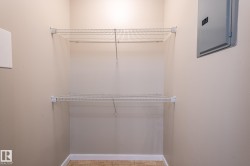 Compact utility space featuring neutral wall paint, two white wire shelving units, a gray electrical panel, and tan tile flooring - 