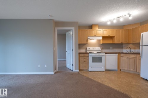 Functional kitchen featuring wood-finish cabinetry, white appliances including a refrigerator, stove, and dishwasher, and track lighting - #314 240 Spruce Ridge Rd, Spruce Grove, AB - Indoor Photo Showing Kitchen