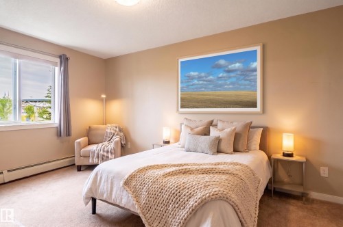 Carpeted bedroom featuring a large window with roller shades, neutral tone walls, and baseboard heating - #314 240 Spruce Ridge Rd, Spruce Grove, AB - Indoor Photo Showing Bedroom