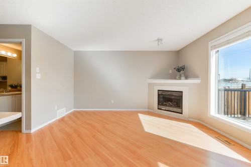 Bright living area featuring wood-finish flooring, a corner fireplace with a white mantel, and a large window - 2923 30 Street, Edmonton, AB - Indoor Photo Showing Living Room With Fireplace