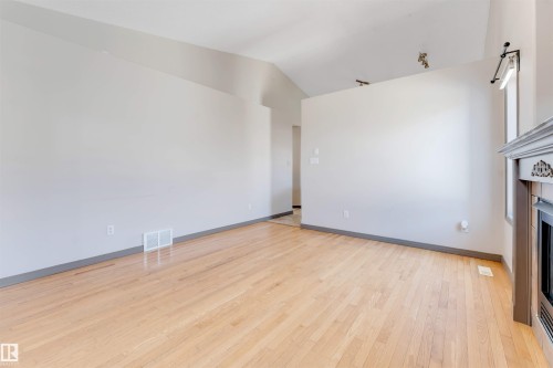 Spacious interior featuring wood-finish flooring, light grey walls, and a vaulted ceiling - 4812 148 Avenue, Edmonton, AB - Indoor Photo Showing Other Room With Fireplace