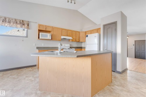 Kitchen featuring light wood cabinetry, a central island with a sink, white appliances, and vaulted ceilings - 4812 148 Avenue, Edmonton, AB - Indoor Photo Showing Kitchen