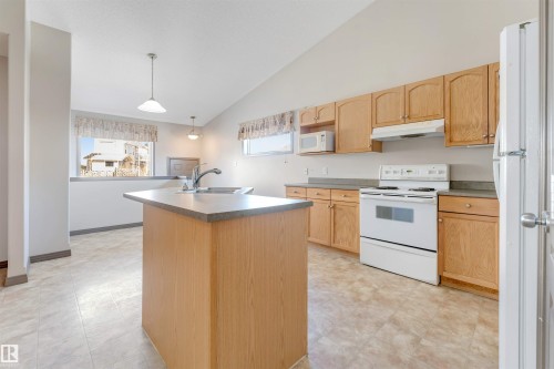 Kitchen featuring a central island with an integrated sink, wood-finish cabinetry, white appliances, and vaulted ceilings - 4812 148 Avenue, Edmonton, AB - Indoor Photo Showing Kitchen