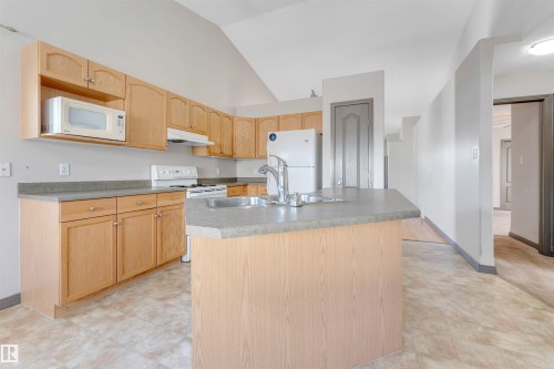 Kitchen featuring light wood cabinetry, stone-finish countertops, stainless steel sink, and durable tile flooring - 4812 148 Avenue, Edmonton, AB - Indoor Photo Showing Kitchen