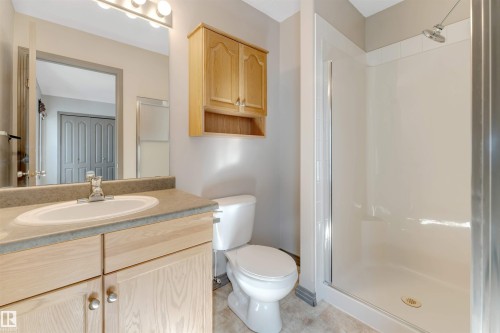 Bathroom featuring a light wood-finish vanity with an integrated sink, a neutral-toned countertop, and a shower stall with a clear glass enclosure - 4812 148 Avenue, Edmonton, AB - Indoor Photo Showing Bathroom
