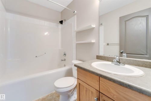 Bathroom featuring a wood-finish vanity with a laminate countertop, an integrated sink, a full-width mirror, and a white tub/shower combination with a grab bar - 4812 148 Avenue, Edmonton, AB - Indoor Photo Showing Bathroom