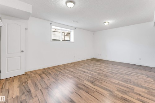 Spacious room featuring wood-finish flooring, white walls, and a window with blinds - 4812 148 Avenue, Edmonton, AB - Indoor Photo Showing Other Room