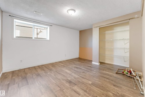 Spacious room featuring wood-finish flooring, a window providing natural light, a ceiling-mounted light fixture, a ceiling vent, and a built-in closet with shelving - 4812 148 Avenue, Edmonton, AB - Indoor Photo Showing Other Room