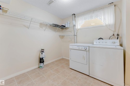 Dedicated utility area featuring a washer and dryer set, wire shelving, a window with blinds, and neutral-toned floor tile - 4812 148 Avenue, Edmonton, AB - Indoor Photo Showing Laundry Room