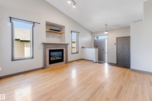 Vaulted ceiling living space featuring a built-in fireplace with a decorative mantel, light wood-finish flooring, recessed shelving, and a prominent entry door - 4812 148 Avenue, Edmonton, AB - Indoor Photo Showing Living Room With Fireplace