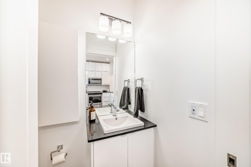 Contemporary vanity with an integrated sink, dark countertop, and modern wall-mounted light fixture - 14812 98 Avenue, Edmonton, AB - Indoor