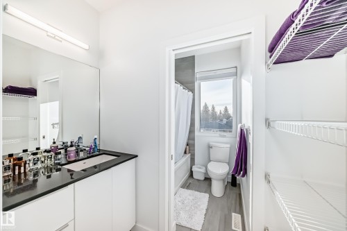 Contemporary bathroom featuring a vanity with a dark countertop and integrated sink, a large wall-mounted mirror, and overhead strip lighting - 14812 98 Avenue, Edmonton, AB - Indoor Photo Showing Bathroom