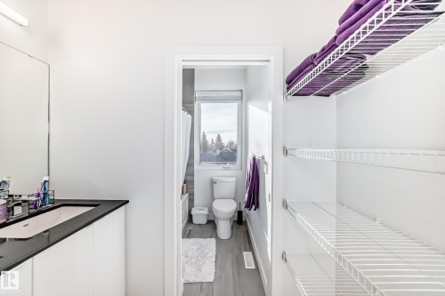Bathroom featuring a vanity with a dark countertop and integrated sink, a wall-mounted mirror, and white wire shelving for storage - 14812 98 Avenue, Edmonton, AB - Indoor
