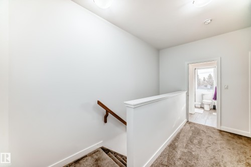 Carpeted hallway with white walls and trim, featuring a wood handrail - 14812 98 Avenue, Edmonton, AB - Indoor Photo Showing Other Room