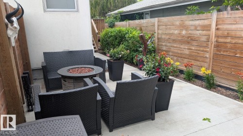 Concrete patio featuring a built-in fire pit, wood privacy fence, and planted garden beds - 14812 98 Avenue, Edmonton, AB - Outdoor With Exterior