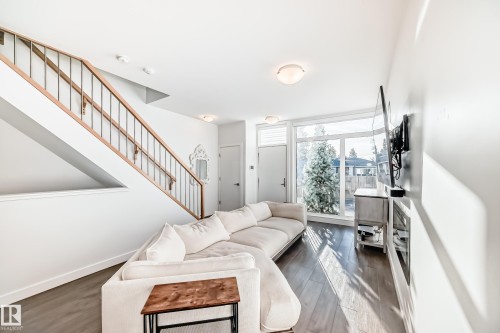 Open-concept living area featuring wood-finish flooring, a contemporary staircase with wood handrails and dark metal spindles, and an expansive window providing natural light - 14812 98 Avenue, Edmonton, AB - Indoor Photo Showing Living Room